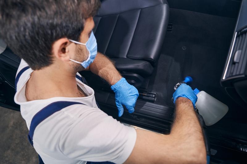 Technician wearing gloves and mask cleaning car interior seats during mobile auto detailing service