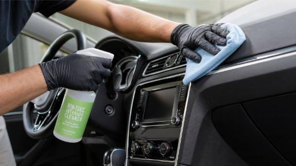 Gloved detailer using non-toxic interior cleaner spray and microfiber cloth to clean car dashboard and steering wheel NYC