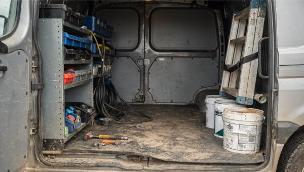 Dirty work van interior before professional deep cleaning service showing tools, shelving, and debris on floor